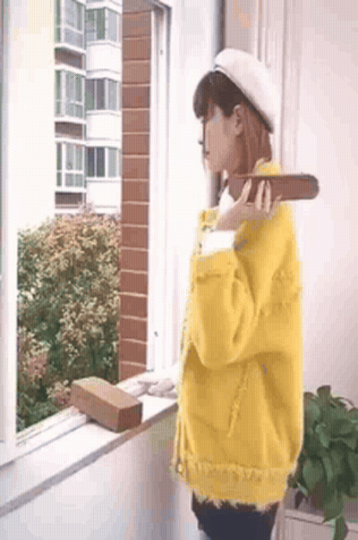 Woman In Yellow Jacket Holding Brick At Window GIF