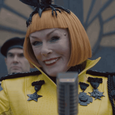 Woman In Yellow Jacket With Medals Smiling At Microphone GIF