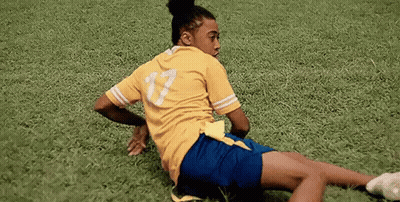 Woman In Yellow Shirt And Blue Shorts Laying On Soccer Field GIF