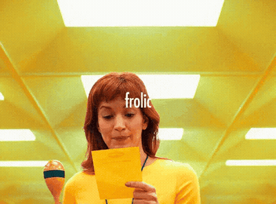 Woman In Yellow Shirt Holding Paper Saying Frolic GIF