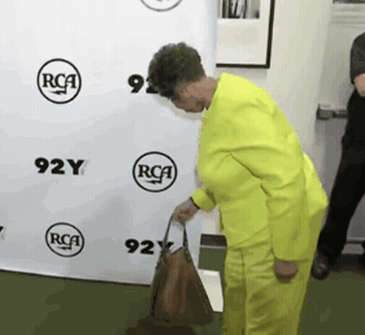 Woman In Yellow Suit Holding Brown Purse GIF