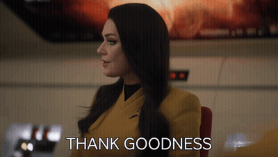 Woman In Yellow Suit Sitting In Front Of Thank Goodness Sign GIF