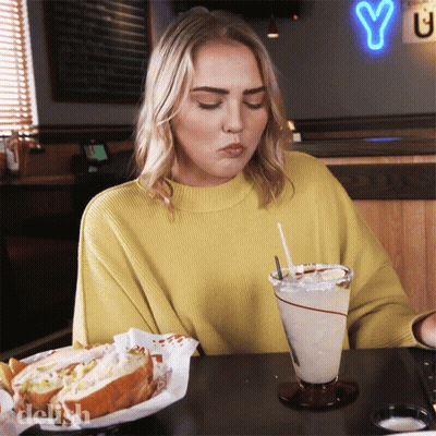 Woman In Yellow Sweater With Sandwich And Drink GIF