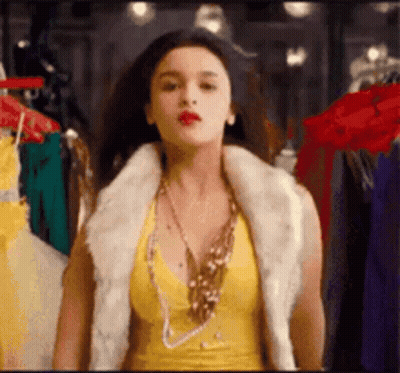 Woman In Yellow Top And Fur Vest By Closet GIF