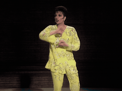 Woman In Yellow Top And Pants Arms Outstretched On Stage GIF