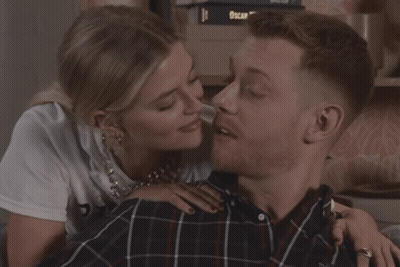 Woman Kissing Man On Cheek In Front Of Oscar Wilde Books GIF