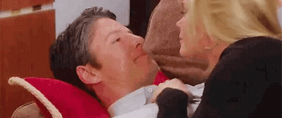 Woman Kissing Man on Cheek While He Lays on Pillow