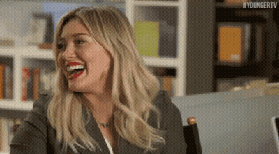 Woman Laughing At Table In Front Of Bookshelf GIF