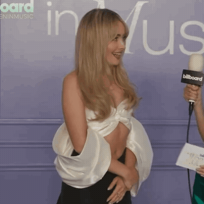 Woman Laughing Holding Microphone In Front Of Billboard GIF