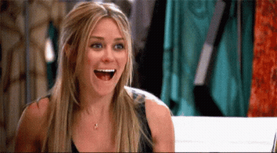 Woman Laughing With Mouth Open Beside Clothes Rack GIF