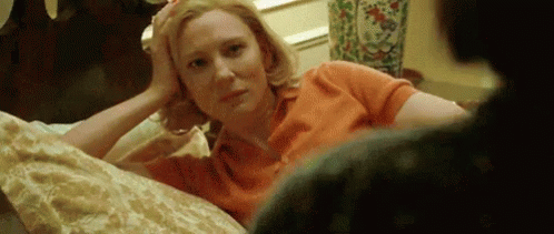 Woman Laying On Bed Hand On Forehead Looking At Camera GIF