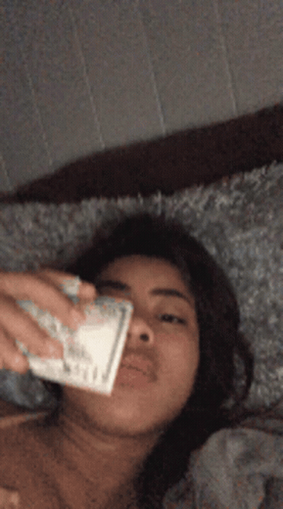 Woman Laying On Bed Holding Money In Mouth GIF