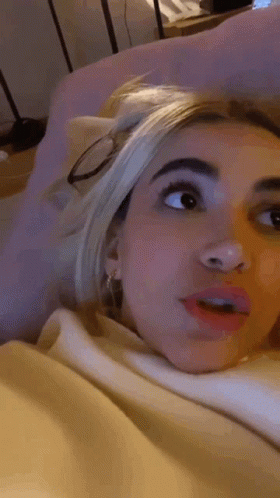 Woman Laying On Bed In Glasses And White Sweater GIF