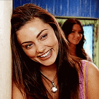 Woman Leaning Against Wall Smiling With Necklace GIF