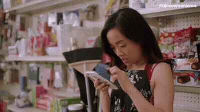 Woman Looking At Cell Phone In Store Aisle GIF