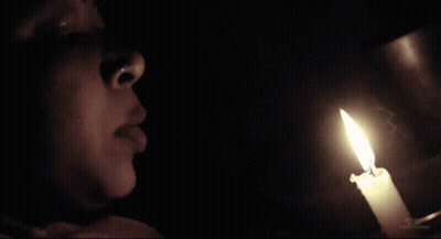 Woman Looking At Lit Candle In Darkness GIF