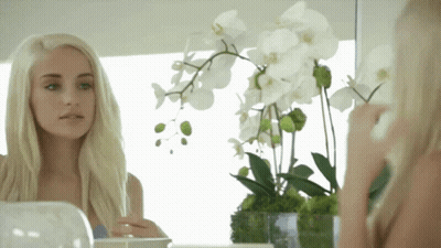 Woman Looking At Reflection In Mirror With Vase Of Flowers GIF
