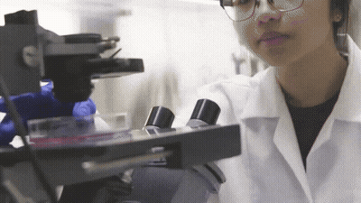 Woman Looking Through Microscope In Lab Coat GIF
