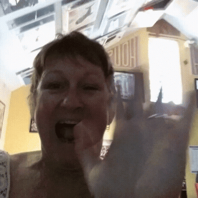Woman Making Horns Sign In Front Of Home Sign GIF