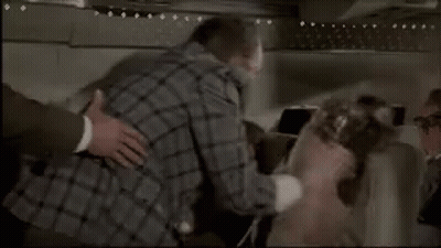 Woman On Airplane Talking To Man In Black Hood GIF