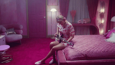 Woman On Bed Playing Guitar In Pink Room GIF