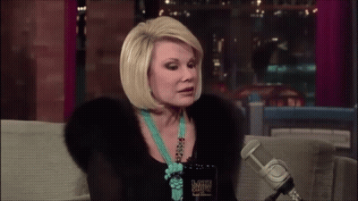 Woman On Couch Talking Into Microphone In Fur Coat And Turquoise Necklace GIF