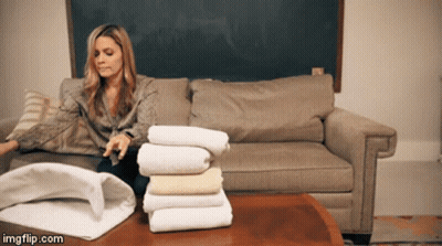 Woman On Couch With Stack Of Towels On Table GIF