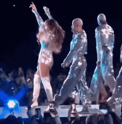 Woman On Stage With Arms Up And People Dancing Behind GIF