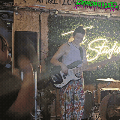 Woman Playing Bass Guitar In Front Of Grindhouse Sign GIF