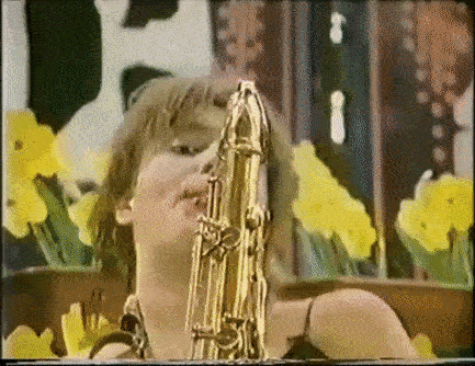 Woman Playing Saxophone In Front Of Yellow Flowers GIF