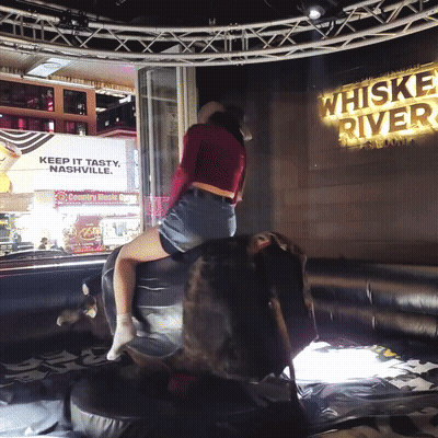 Woman Riding Bull Near Whiskey River Sign GIF