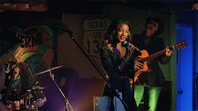 Woman Singing In Front Of Texas Sign GIF