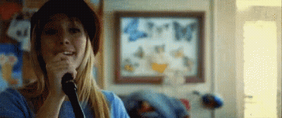 Woman Singing Into Microphone In Front Of Butterfly Painting GIF