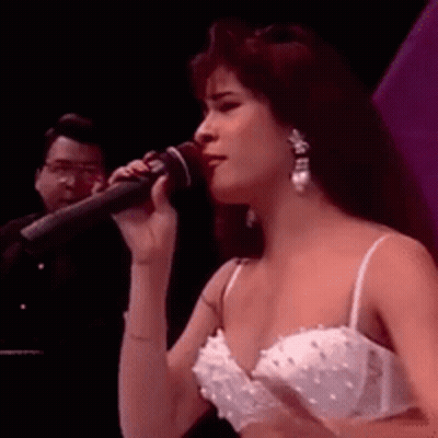 Woman Singing Into Microphone In White Dress And Earrings GIF