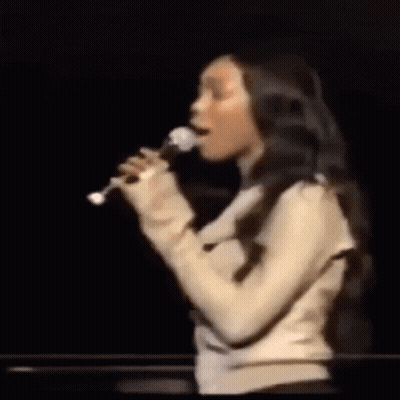 Woman Singing Into Microphone On Dark Stage GIF