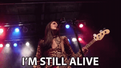 Woman Singing Into Microphone Playing Guitar Saying I'm Still Alive GIF