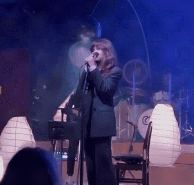 Woman Singing Into Microphone With Drum Set GIF