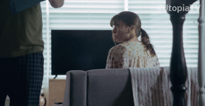 Woman Sits On Couch In Front Of TV With Hashtag Utopiatv GIF