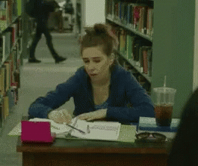 Woman Sitting At Desk In Library With Coffee GIF