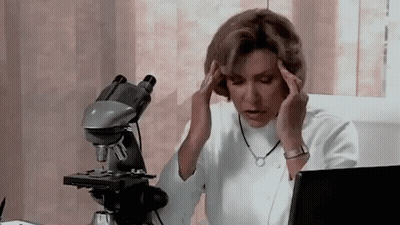 Woman Sitting At Microscope Holding Head GIF