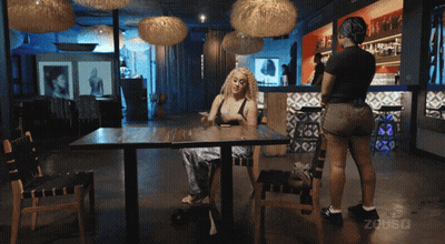 Woman Sitting At Restaurant Table With Woman Behind GIF