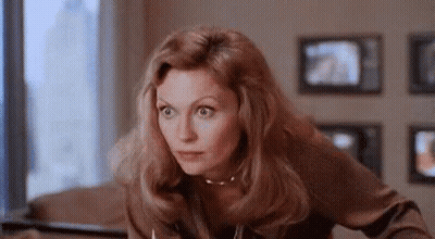 Woman Sitting At Table In Front Of TV Looking At Camera GIF
