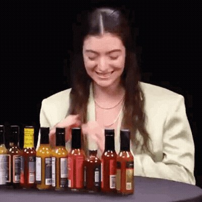 Woman Sitting At Table With Hot Sauce Bottles GIF