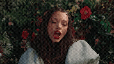 Woman Sitting In Field Of Flowers With Red Lipstick GIF