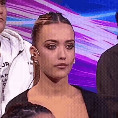 Woman Sitting In Front Of Crowd Looking At Camera GIF