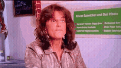 Woman Sitting In Front Of Finest Sandwiches And Deli Meats Sign GIF