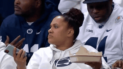 Woman Sitting In Stands Holding Tray Of Food And Phone GIF