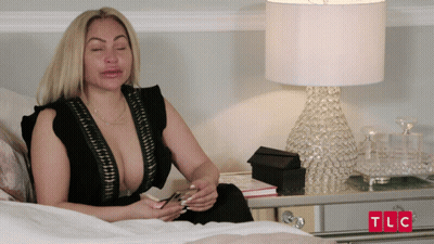 Woman Sitting On Bed Next To Lamp With TLC In Red Letters GIF