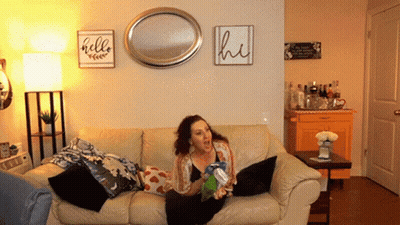 Woman Sitting On Couch In Front Of Hello And Hi Sign GIF