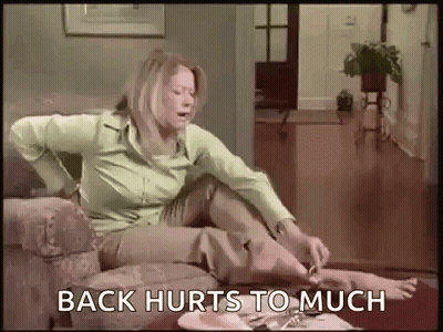 Woman Sitting On Couch In Pain Saying Back Hurts Too Much GIF